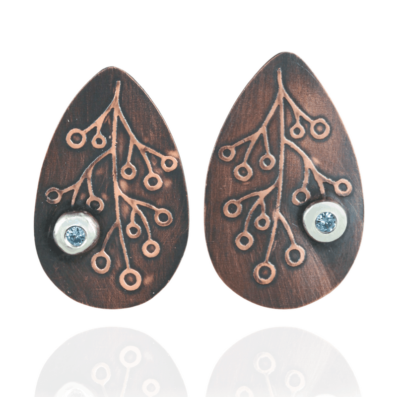 Teardrop-shaped earrings with intricate botanical designs and blue zirconia gemstones on a white background.