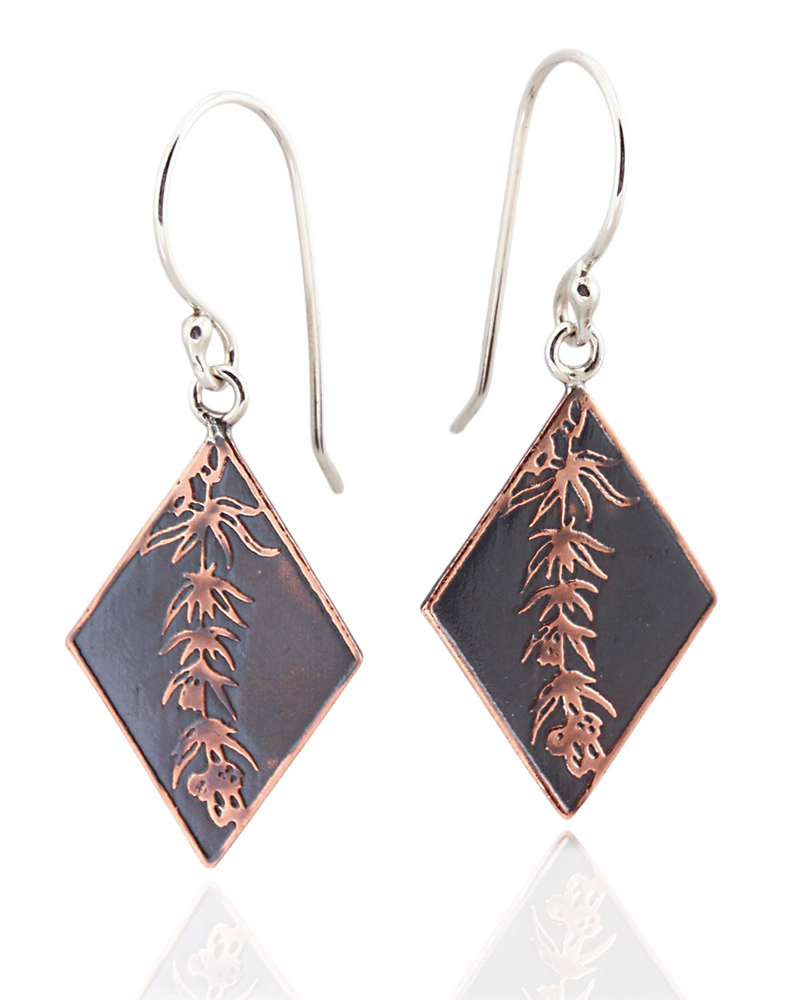 Pair of diamond-shaped earrings with floral vine design on the front on a white background.