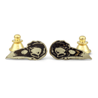 Pair of gold and black crow skull-shaped pins on a white background