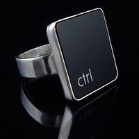 A silver ring featuring a black vertical rectangle with the lowercase letters 'ctrl', photographed on a reflective black surface.