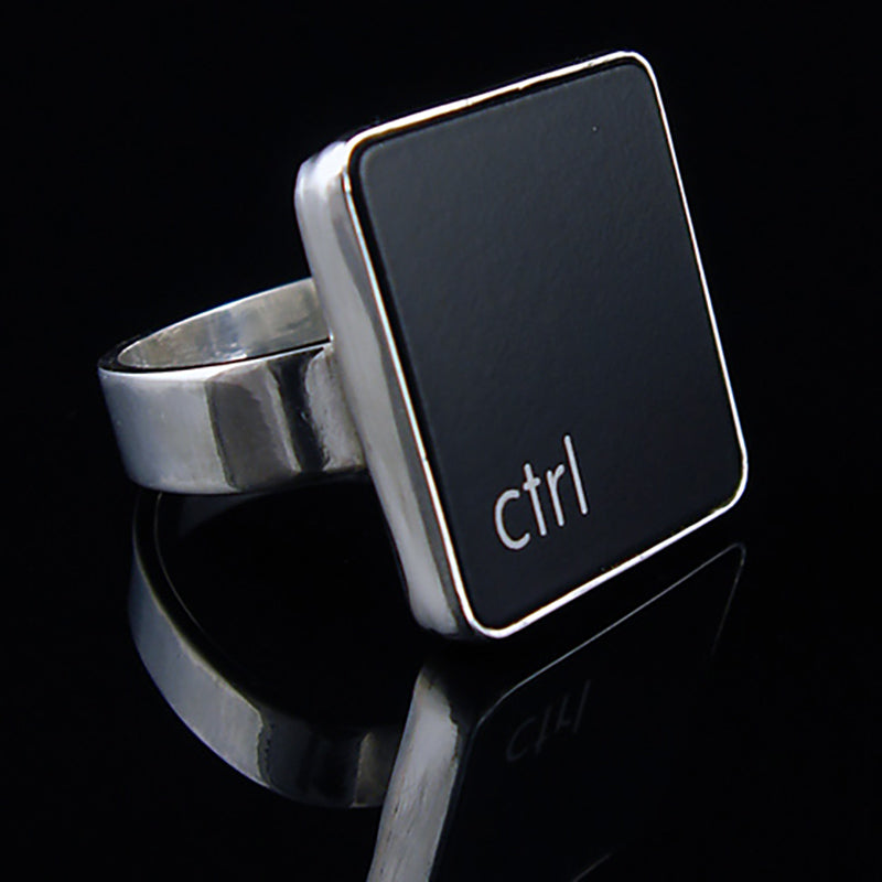 A silver ring featuring a black vertical rectangle with the lowercase letters 'ctrl', photographed on a reflective black surface.