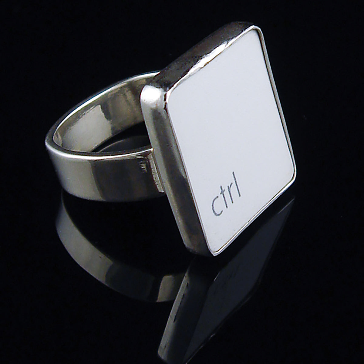 A silver ring featuring a white vertical rectangle with the lowercase letters 'ctrl', photographed on a reflective black surface.