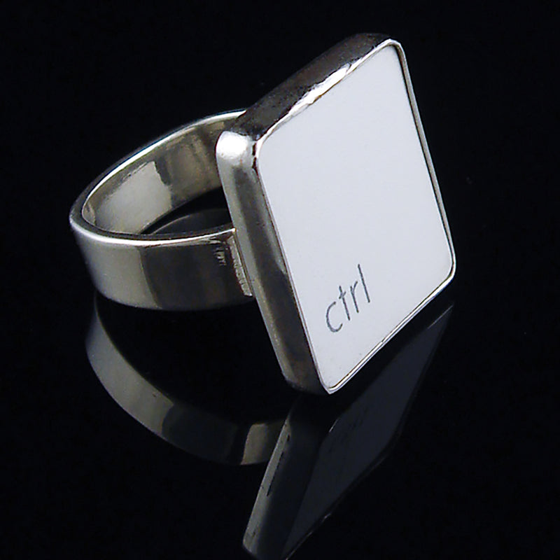 A silver ring featuring a white vertical rectangle with the lowercase letters 'ctrl', photographed on a reflective black surface.