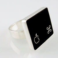 A silver ring featuring a black square with white Apple logo and command symbol, photographed on a clean white background.