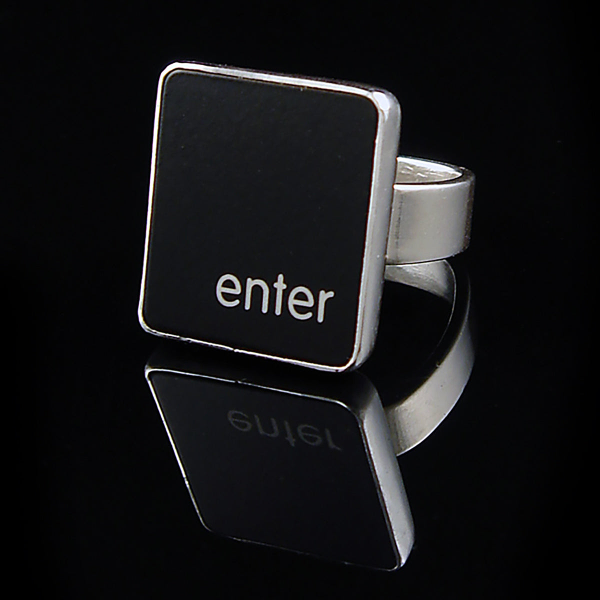 A silver ring featuring a black vertical rectangle with the lowercase letters 'enter', photographed on a reflective black surface.