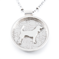 A silver round pendant necklace featuring a beagle dog silhouette over a jigsaw bone pattern, suspended from a silver chain on a white background.
