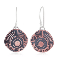 Copper and silver earrings with circular ray design on a white background