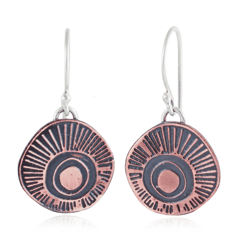 Copper and silver earrings with circular ray design on a white background