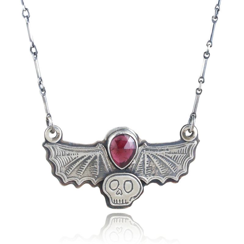 Pendant with a luscious red teardrop garnet surrounded by bat wings and a skull on a white background.