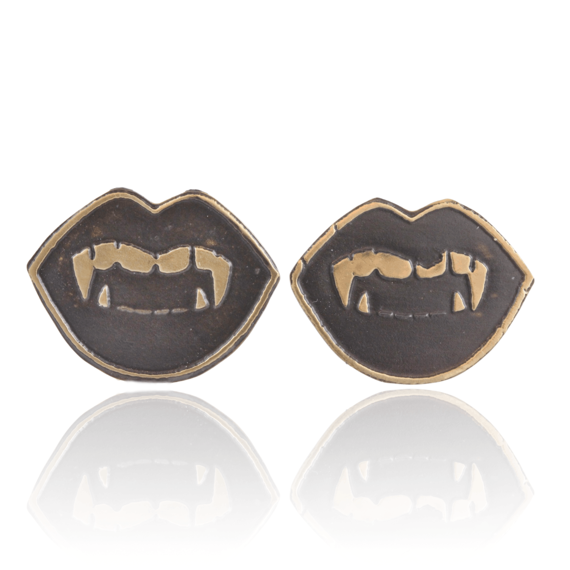 Pair of gold oxidized metal vampire fang lip shaped earrings on a white background