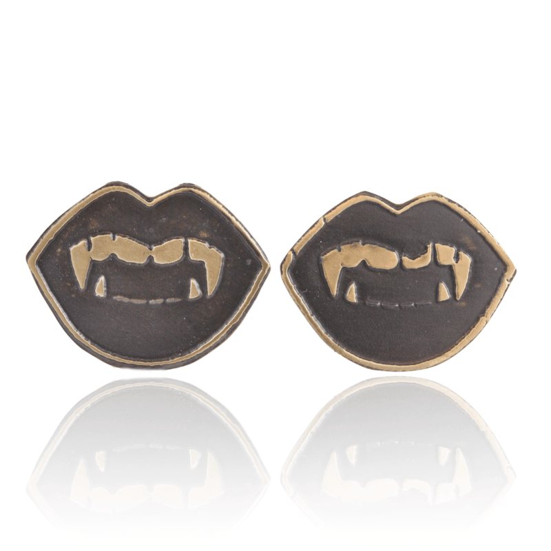 Pair of gold oxidized metal vampire fang lip shaped earrings on a white background