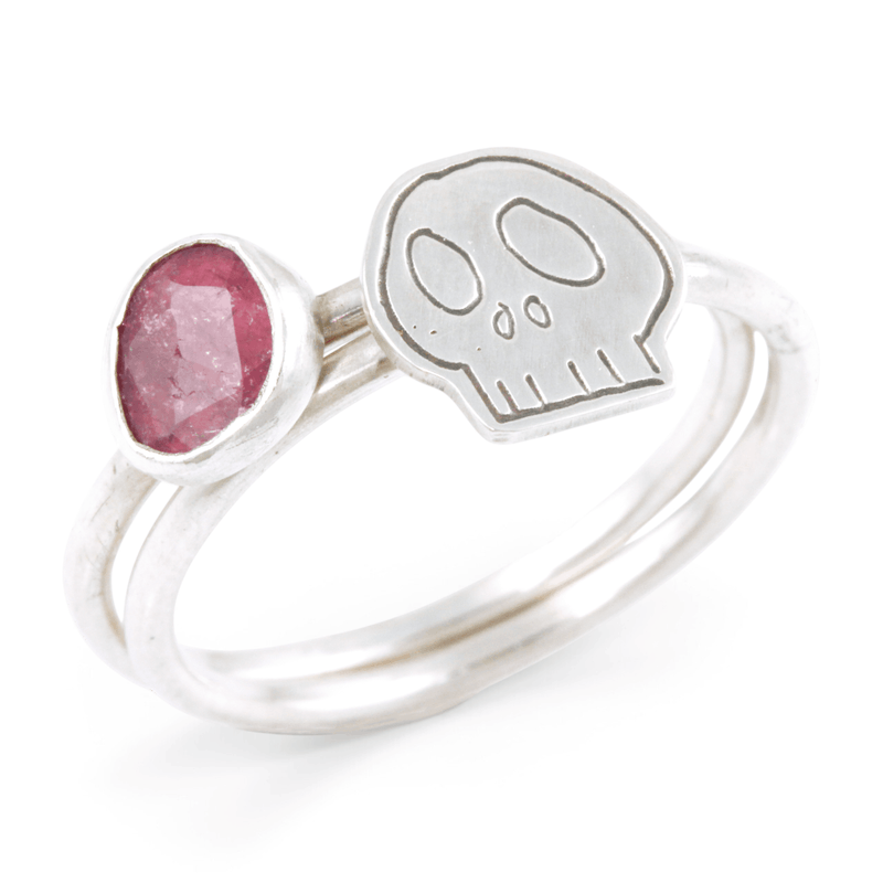 Two silvers ring together, featuring one with a pink gemstone and the other with an engraved skull motif, set against a clean white background.
