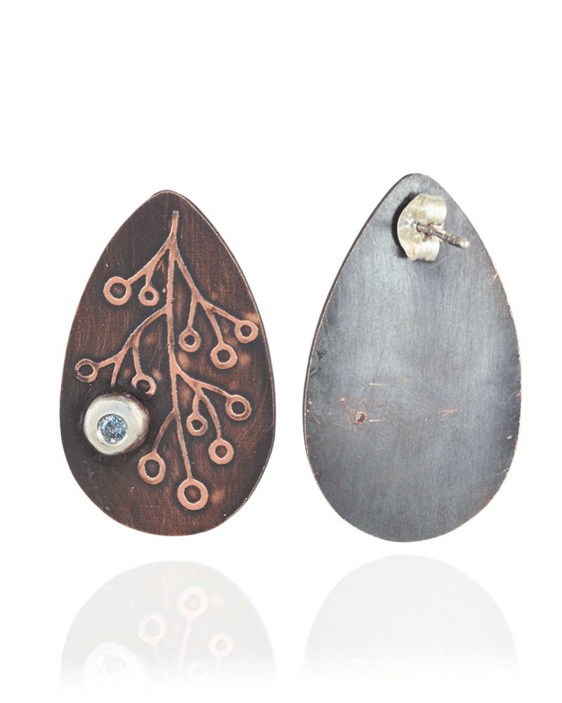 Teardrop-shaped earrings with intricate botanical designs and blue zirconia gemstones on a white background.