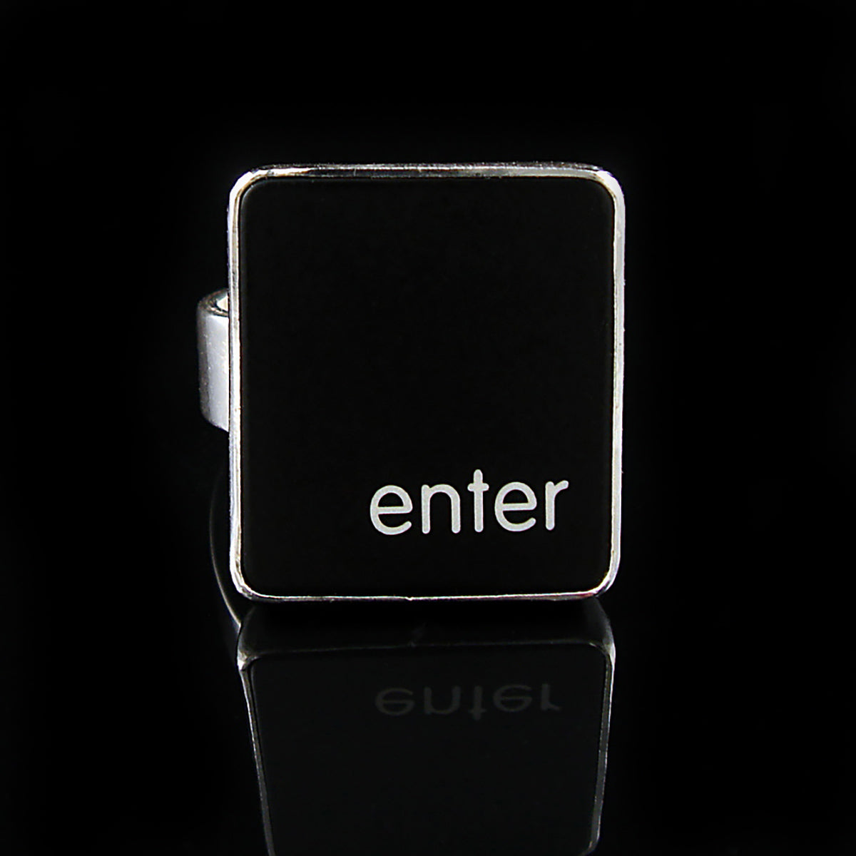 A silver ring featuring a black vertical rectangle with the lowercase letters 'enter', photographed on a reflective black surface.