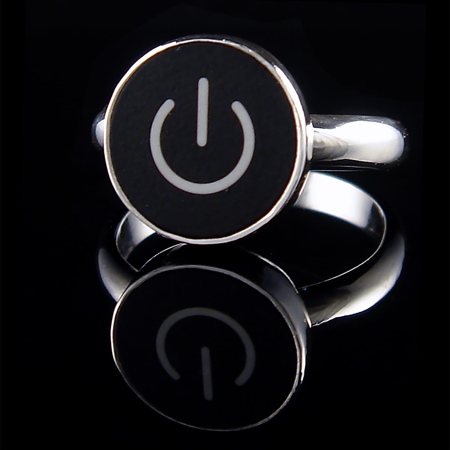 A silver ring featuring a round black face with a white on/off symbol, displayed on a reflective black surface.