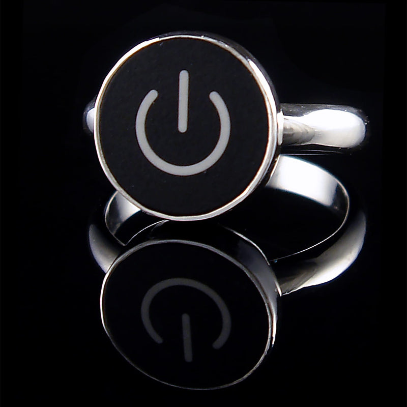 A silver ring featuring a round black face with a white on/off symbol, displayed on a reflective black surface.