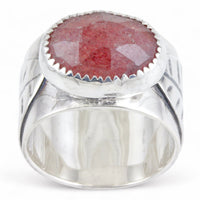 A sterling silver ring featuring a large, oval, faceted reddish-pink gemstone in a textured bezel setting, and a leaf on the ring band, shown on a plain white background.