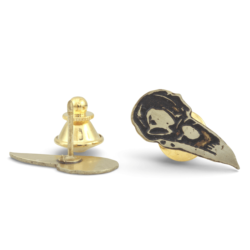 Pair of gold and black crow skull-shaped pins on a white background