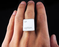 A close-up of a hand wearing a silver ring featuring a white vertical rectangle with the words 'alt option' printed in white lowercase text.