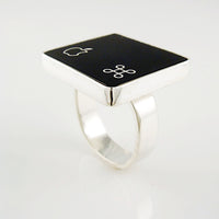 A silver ring featuring a black square with white Apple logo and command symbol, photographed on a clean white background.