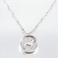 A silver round pendant necklace featuring a beagle dog silhouette over a jigsaw bone pattern, suspended from a silver chain on a reflective grey background.