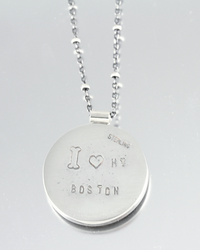 A sterling silver round pendant necklace engraved with 'I Heart MY BOSTON' and 'STERLING', shown on a light gray reflective surface.