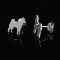 A pair of silver stud earrings shaped like a small dog, shown on a reflective black background. One earring is facing forward, and the other is turned to show the post and butterfly back.