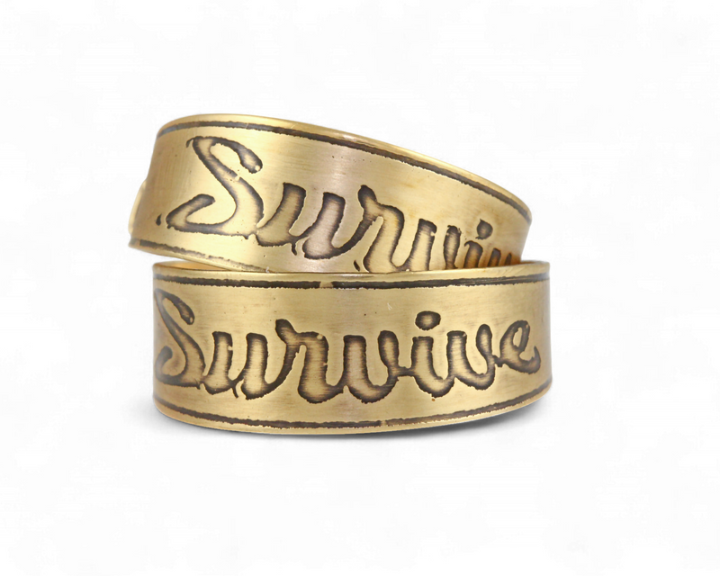 Two nu-gold brass rings with 'Survive' engraved on a white background