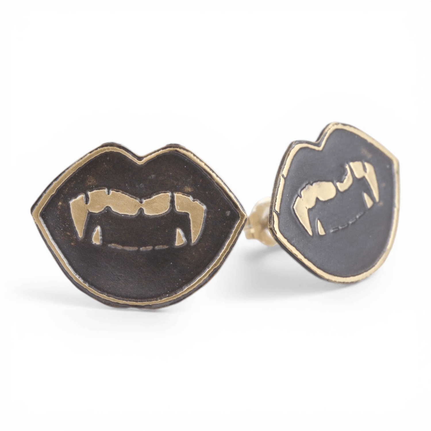 Pair of gold oxidized metal vampire fang lip shaped earrings on a white background