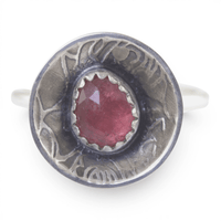 A sterling silver ring featuring a round, rose pattern textured dome set with a faceted pinkish-red gemstone, shown on a plain white background.