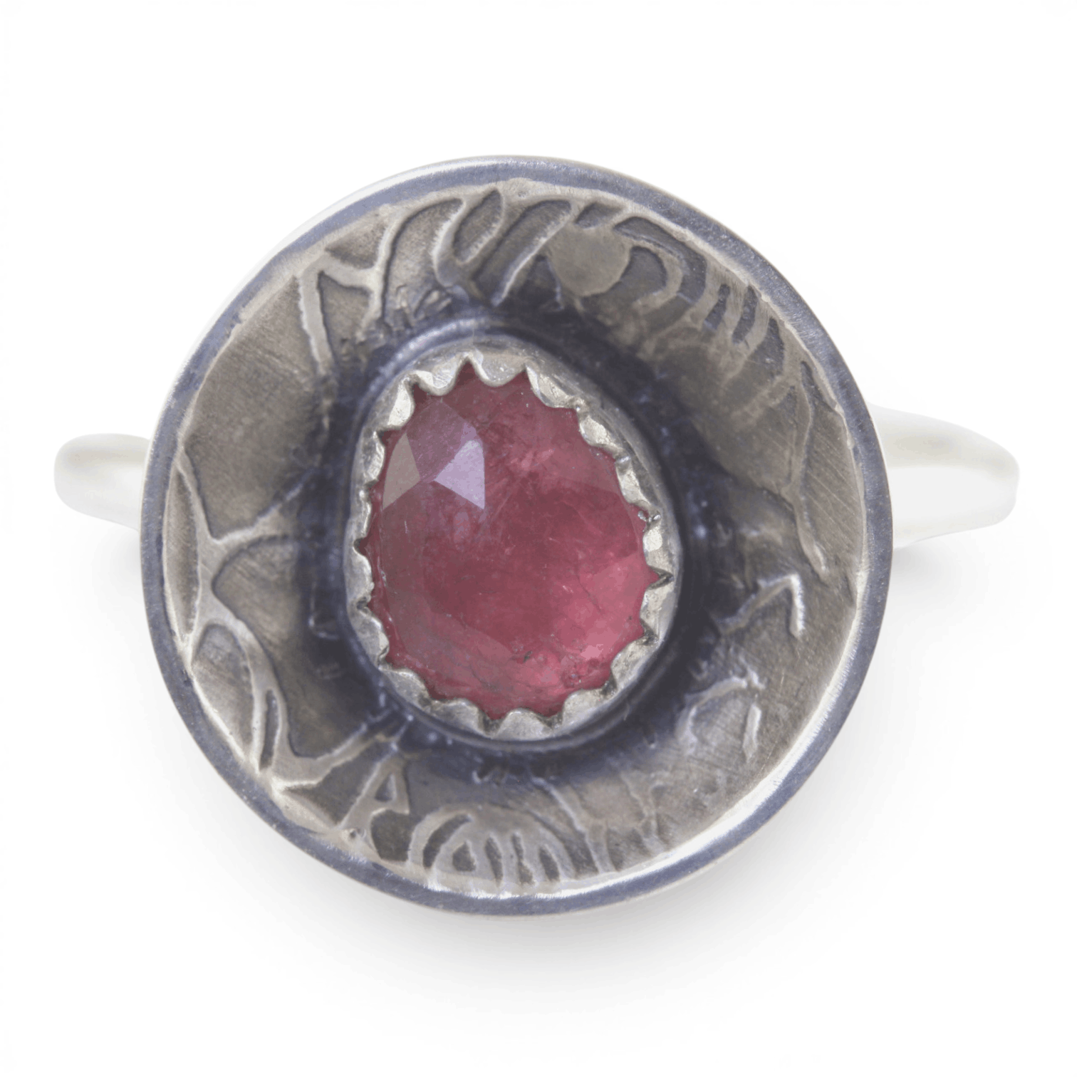 A sterling silver ring featuring a round, rose pattern textured dome set with a faceted pinkish-red gemstone, shown on a plain white background.