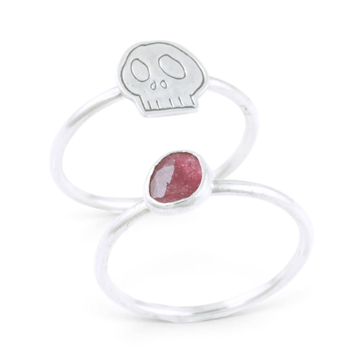Two silvers ring together, featuring one with a pink gemstone and the other with an engraved skull motif, set against a clean white background.