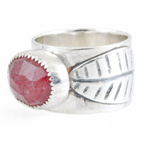 A sterling silver ring featuring a large, oval, faceted reddish-pink gemstone in a textured bezel setting, and a leaf on the ring band, shown on a plain white background.