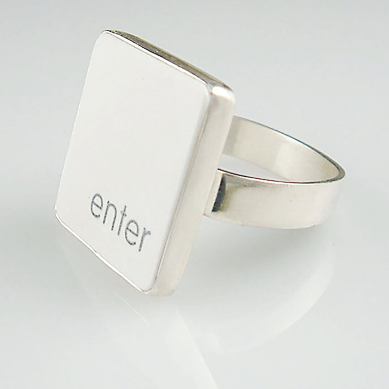 A silver ring featuring a white vertical rectangle with the lowercase letters 'enter', shown on a clean white reflective surface.