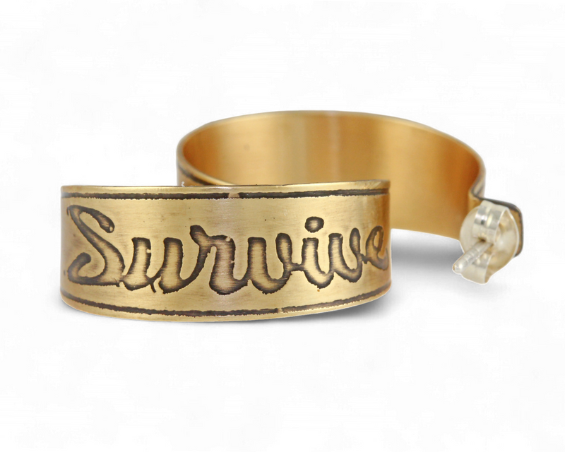 Handmade nu-gold brass hoop earrings with engraved 'Survive' design on a white background.