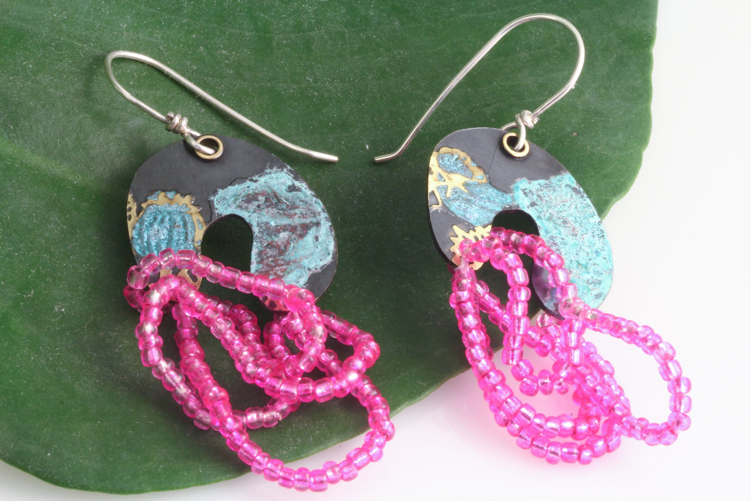 Colorful arch shaped dangle earrings with hot pink beads on a natural green leaf and white background.