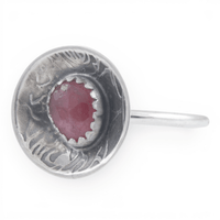 A sterling silver ring featuring a round, rose pattern textured dome set with a faceted pinkish-red gemstone, shown on a plain white background.