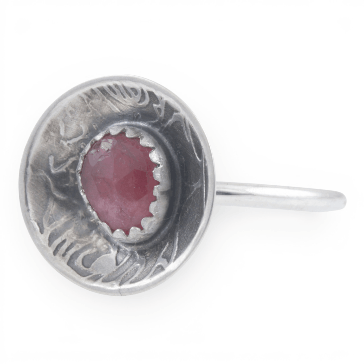 A sterling silver ring featuring a round, rose pattern textured dome set with a faceted pinkish-red gemstone, shown on a plain white background.