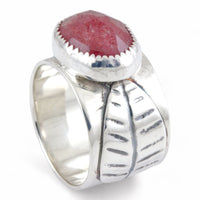 A sterling silver ring featuring a large, oval, faceted reddish-pink gemstone in a textured bezel setting, and a leaf on the ring band, shown on a plain white background.