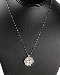 A silver coin pendant necklace featuring a beagle dog motif, displayed on a black textured jewelry bust.