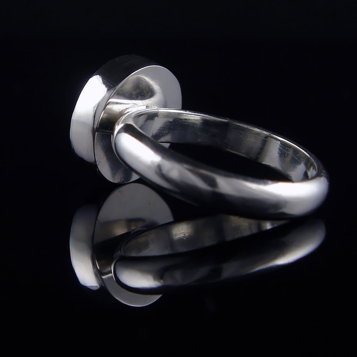 A polished silver metal ring with a wide, circular flat top, photographed on a reflective black surface.