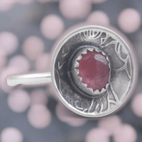 Silver ring with a red gemstone on a blurred pink bubble background