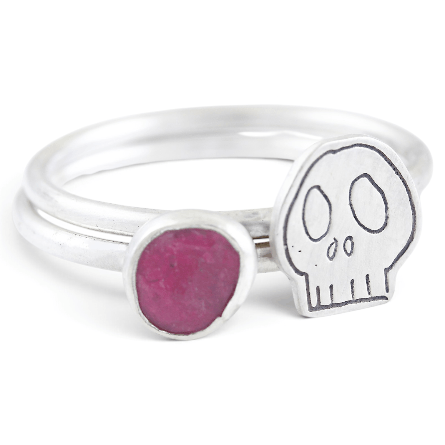 Two silvers ring together, featuring one with a pink gemstone and the other with an engraved skull motif, set against a clean white background.