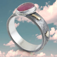 Silver ring with gold and a pink stone against a pink daydreaming cloudy sky background