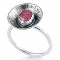 A sterling silver ring featuring a round, rose pattern textured dome set with a faceted pinkish-red gemstone, shown on a plain white background.