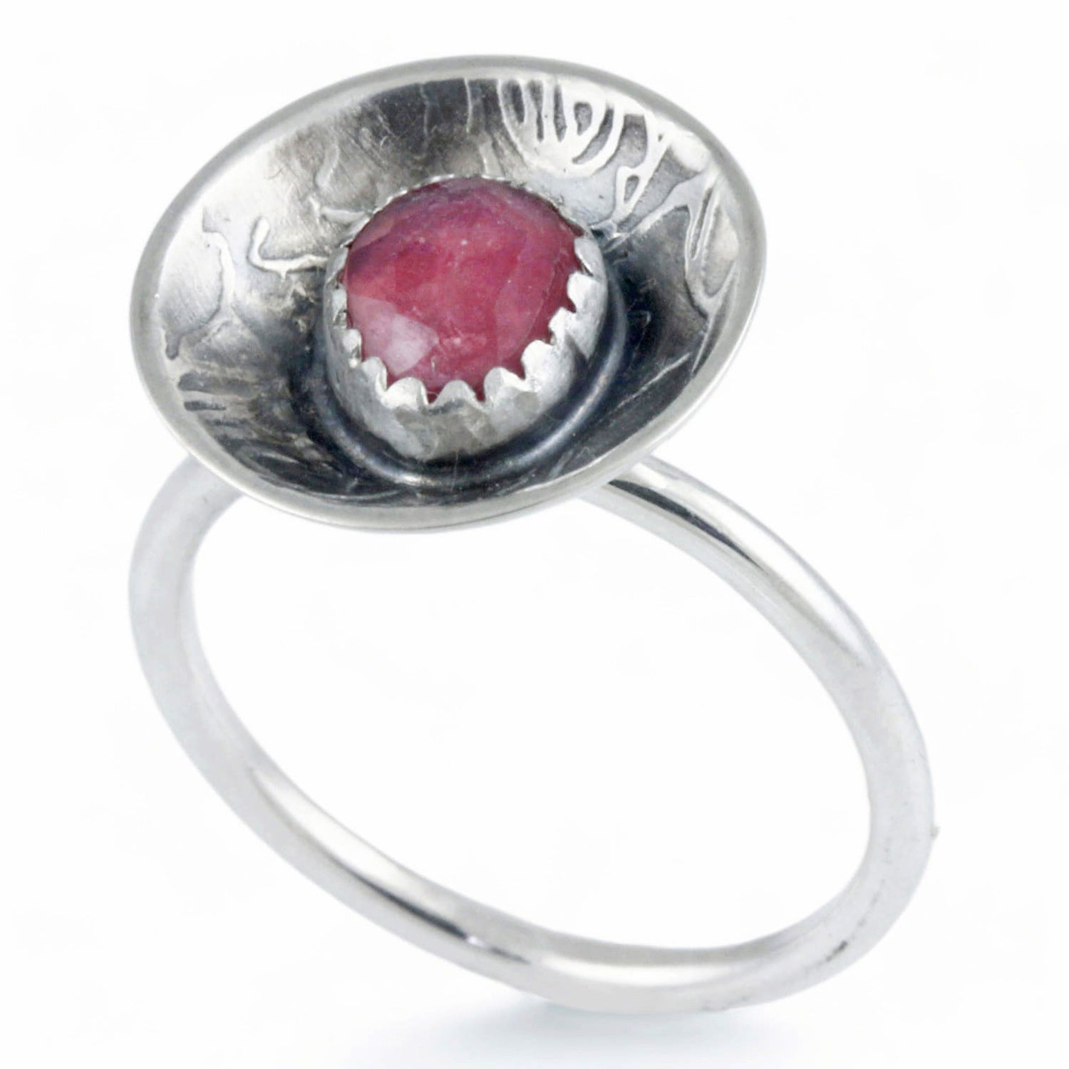 A sterling silver ring featuring a round, rose pattern textured dome set with a faceted pinkish-red gemstone, shown on a plain white background.