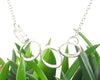 Sterling silver abstract oval necklace with hand-forged satin finish pendant and magnetic clasp on 20-inch cable chain displayed on green leaves