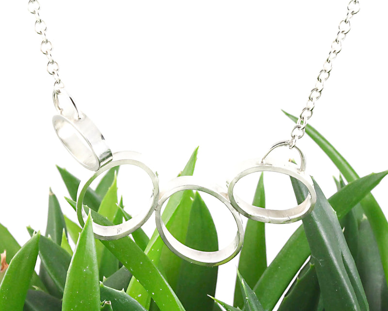 Sterling silver abstract oval necklace with hand-forged satin finish pendant and magnetic clasp on 20-inch cable chain displayed on green leaves