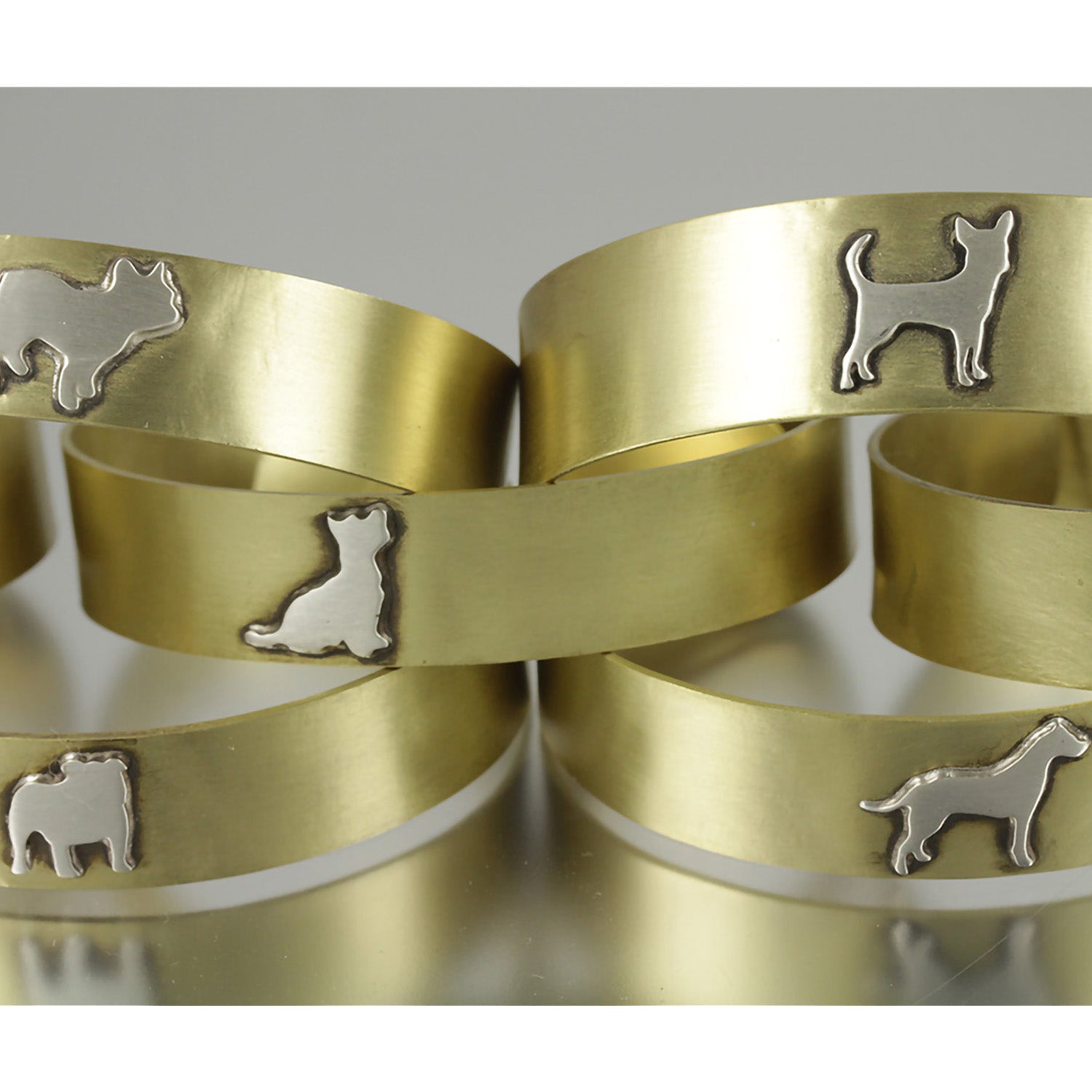 Five stacked adjustable brass cuffs with various .925 sterling silver dog breed silhouette on them.