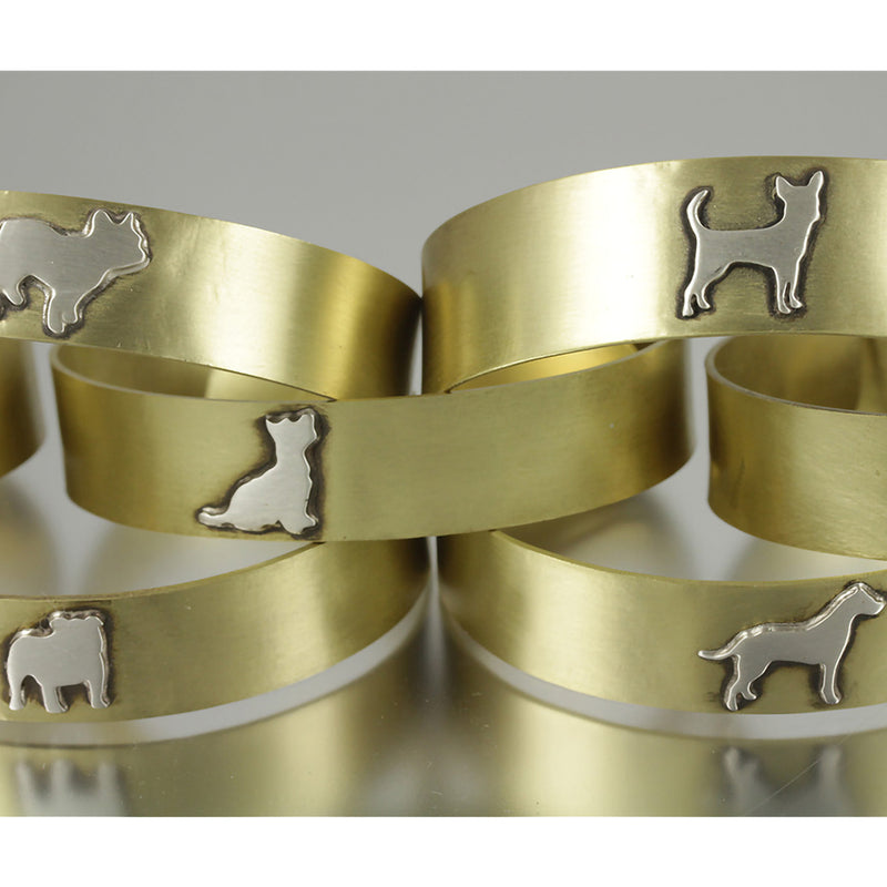 Five stacked adjustable brass cuffs with various .925 sterling silver dog breed silhouette on them.
